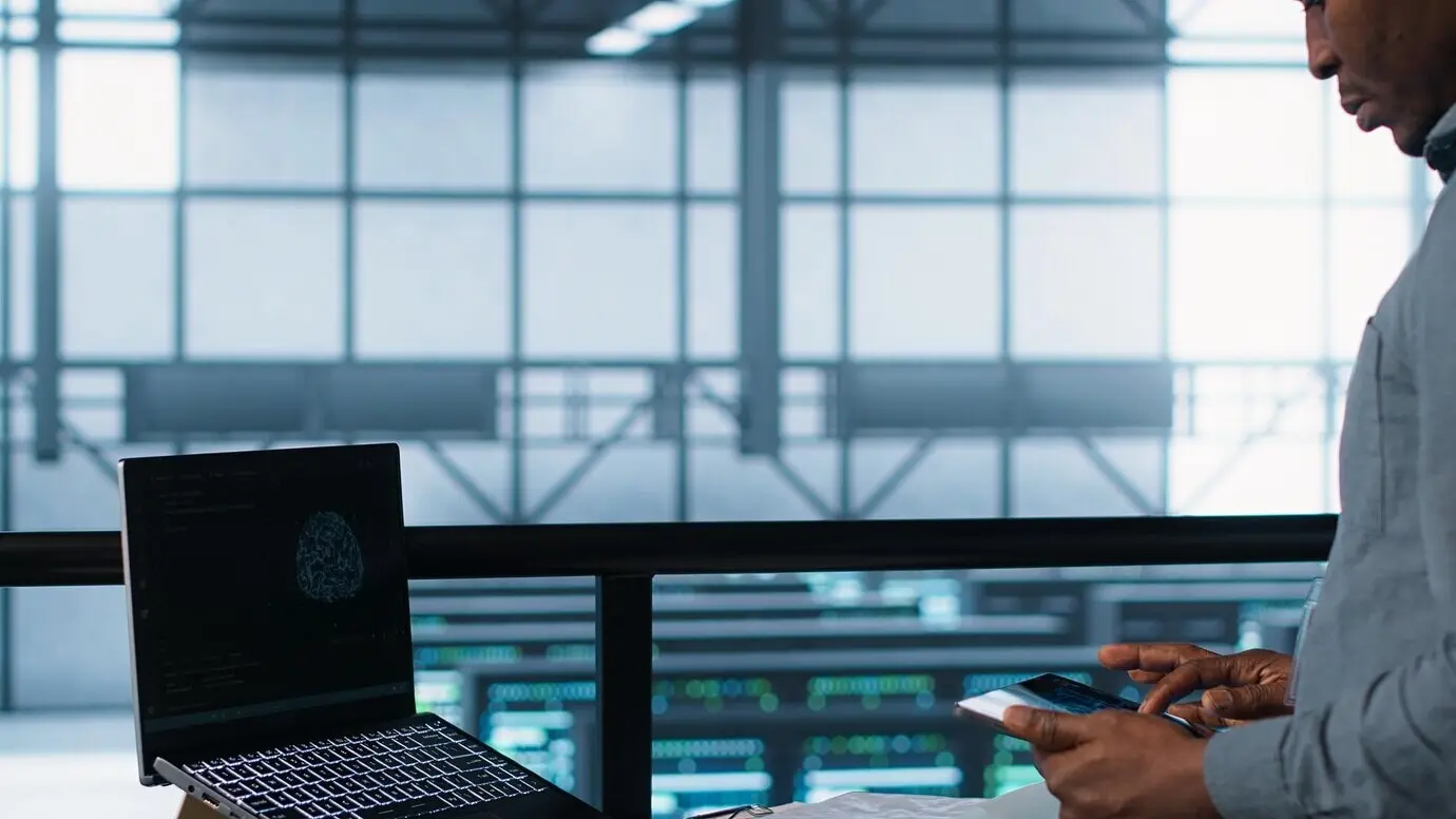 Техник в центре обработки данных с ноутбуком и планшетом, интегрирующий технологии ИИ.